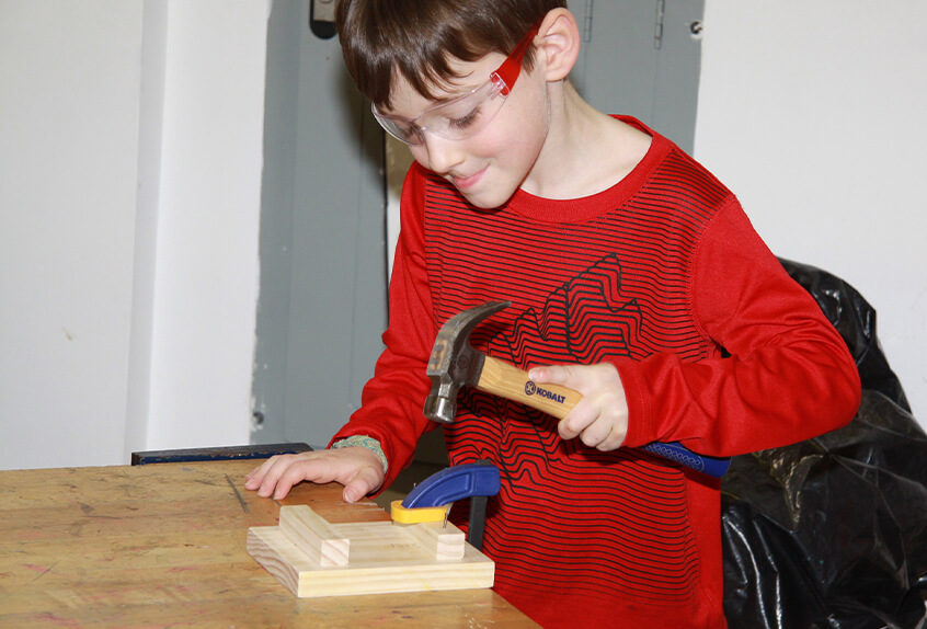 Lower school student learning to safely hammer nails