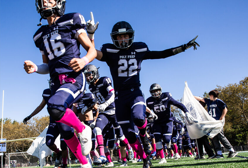 Poly Prep Varsity Football Team breaking through a banner at the Homecoming game