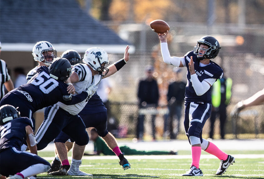 Poly Prep Varsity Football Quarterback throwing the ball as defense holds off the other team