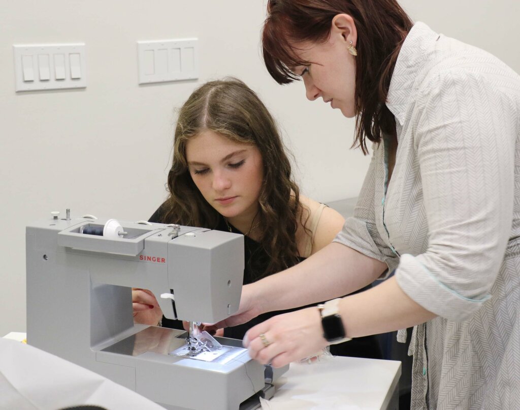 teacher showing student sewing machine technique